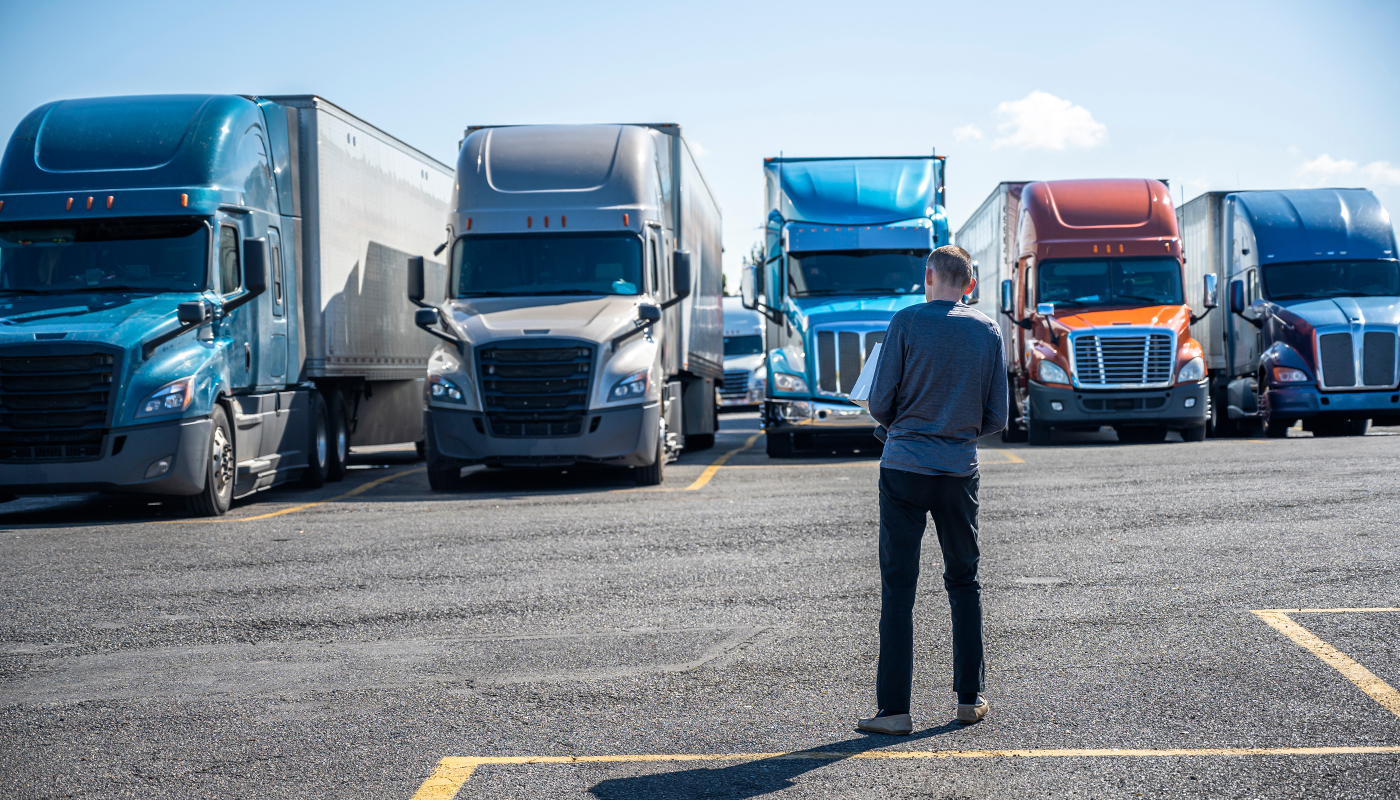 A man looking over semi truck in a row in a parking lot