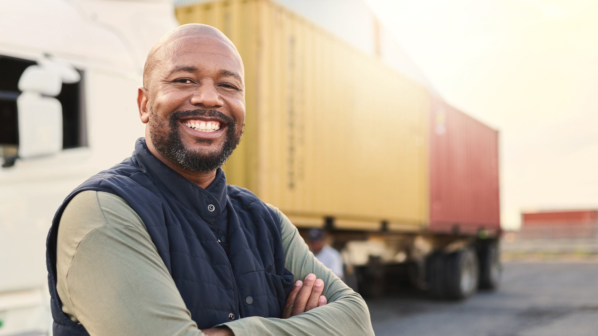 A driver or carrier with arms crossed standing outside a semi truck trailer
