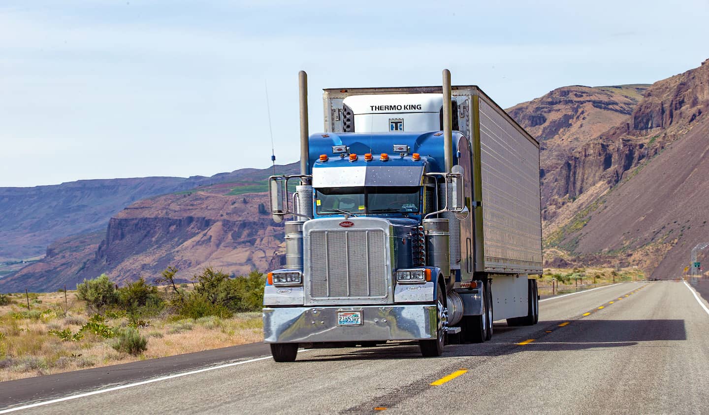 Blue semi-truck driving on the highway in the mountains.