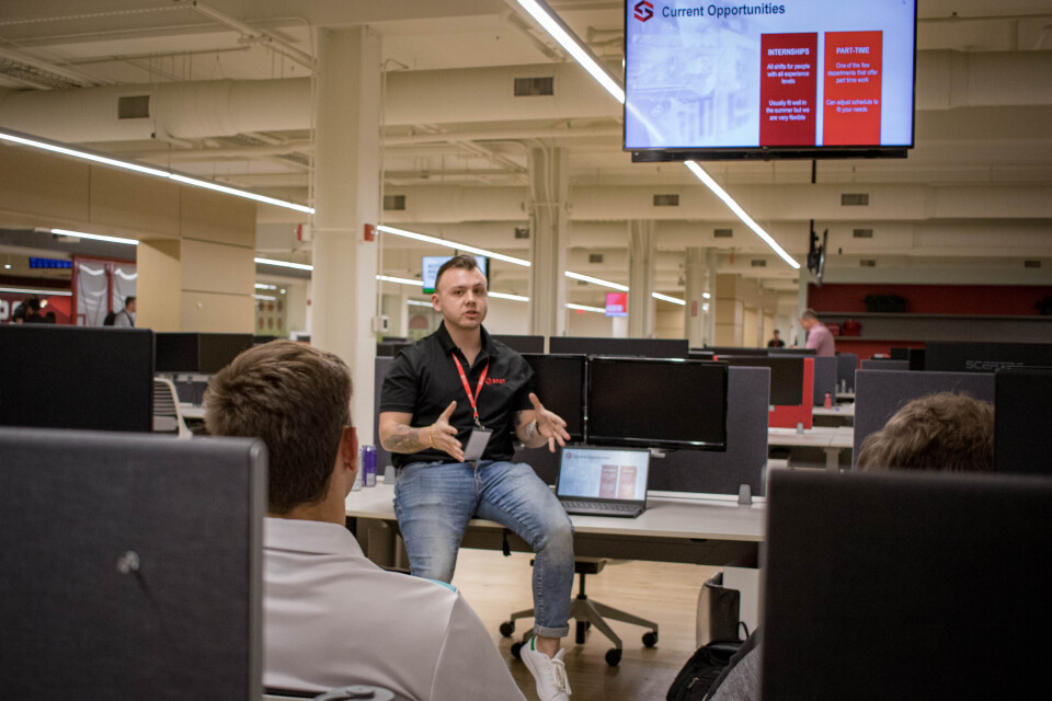 Spot employee sitting on a desk speaking to a group of people.