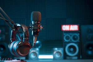 Radio station microphone with headphones in the foreground and speakers in the background with red On Air sign