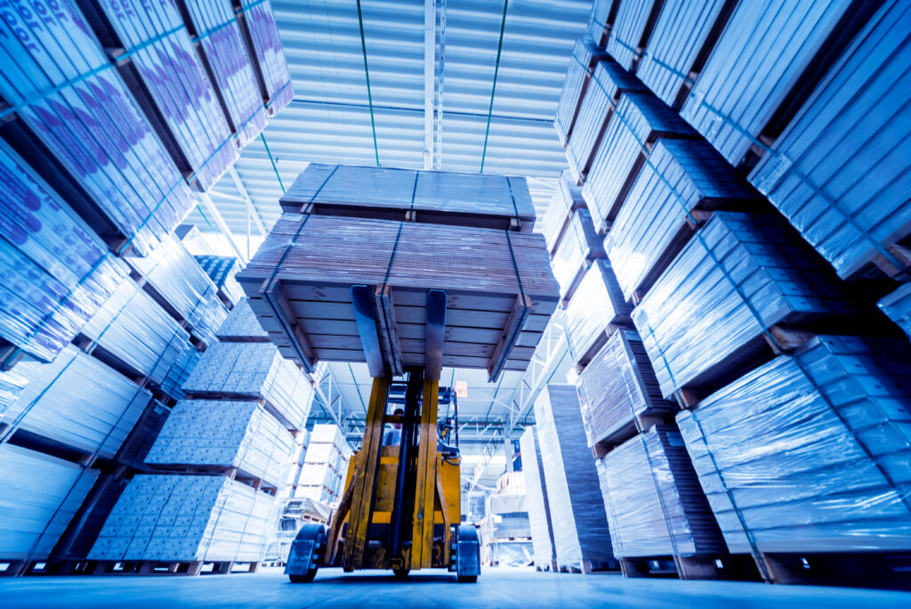 Blue hue of inside of warehouse with a yellow forklift raising pallets