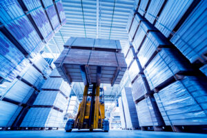 Blue hue of inside of warehouse with a yellow forklift raising pallets