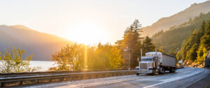 An American semi truck drives on a highway in the mountains at sunset