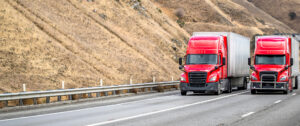 2 red American semi trucks on a highway in the mountains