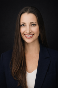 Portrait of white woman with long black hair, white shirt and navy blue sport jacket